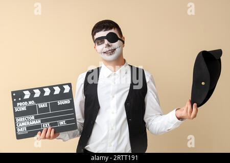 Hübscher junger Mann, der zu Halloween als Pirate mit Klapperbrett auf beigem Hintergrund gekleidet ist Stockfoto