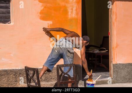 Trinidad, Kuba am 30. Dezember 2015: Ein Mann bemalt eine Wand mit einer leuchtend orangen Farbe. Dies veranschaulicht die Neulackierung Kubas in einem politischen Stockfoto