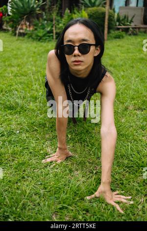 Eine asiatische Frau mit Sonnenbrille und einem schwarzen Hemd, die auf dem grünen Gras posiert und krabbelt Stockfoto