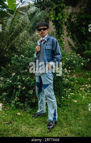 Ein asiatischer Mann mit Sonnenbrille und einem Jeanshemd, der mittags vor einer blühenden Pflanze steht Stockfoto