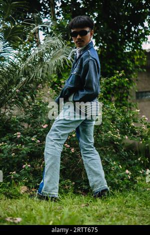 Ein asiatischer Mann, der sich am Morgen in einem Wald mit seiner Jeanssonnenbrille sehr exzentrisch ausgibt Stockfoto