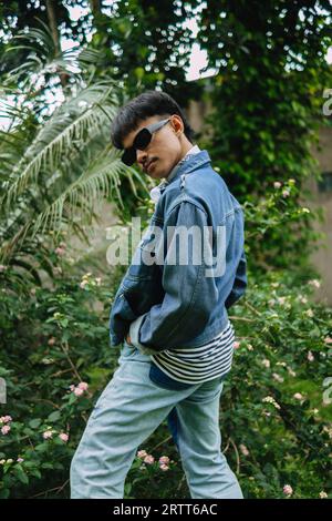 Ein asiatischer Mann, der sich am Morgen in einem Wald mit seiner Jeanssonnenbrille sehr exzentrisch ausgibt Stockfoto