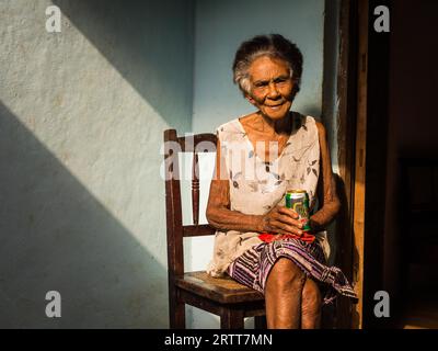 Baracoa, Kuba am 7. Januar 2016: In einem kubanischen Haus genießt eine alte Frau ein Bier in der Sonne Stockfoto