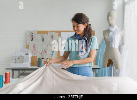 Die asiatische Modedesignerin bewundert ihr Handwerk in akribischer Vorbereitung unter bunten Stoffen in ihrem kreativen Paradies. Stockfoto