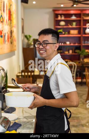 Vietnamesischer Küchenchef in einem einheitlichen Löffel und einer Schüssel mit flüssigem Teig für belgische Waffeln Stockfoto