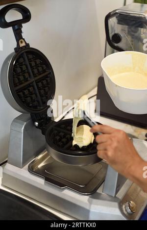 Der Koch gibt den Teig für süße Waffeln mit einem Löffel in das Waffeleisen Stockfoto