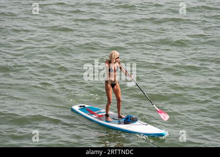 Weibliche Paddelboarderin trägt Bikini während der heißen September-Hitzewelle, Paddleboarding auf der Themse Estuary vor Southend on Sea, Essex, UK Stockfoto