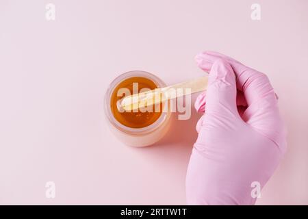 Goldene Zuckerpaste oder Wachs zum Epilieren auf rosafarbenem Hintergrund. Zucker und Enthaarung. Stockfoto