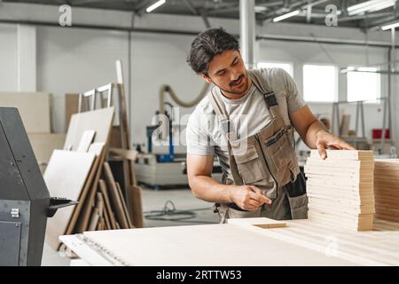 Junger Zimmermann sucht und wählt Holzbohle in einer Werkstatt in einer Holzfabrik Stockfoto