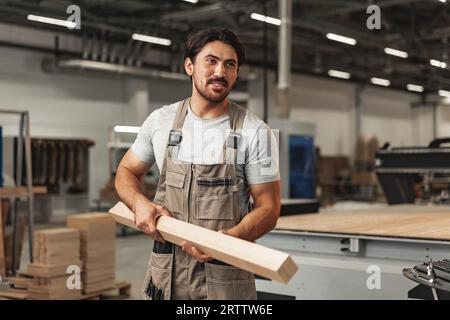 Junger Zimmermann sucht und wählt Holzbohle in einer Werkstatt in einer Holzfabrik Stockfoto