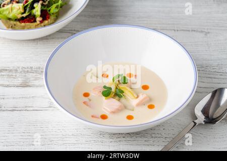 Lachssuppe auf einem weißen Porzellanteller mit Salat an der Seite Stockfoto