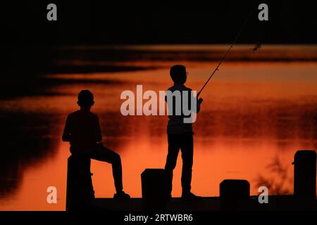 Junge Silhouette auf Pier Angeln im See während der goldenen Stunde Stockfoto