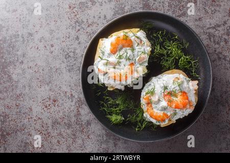 Gebackene Kartoffeln, gefüllt mit Sauerrahmsauce, Knoblauch, Dill und Garnelen aus nächster Nähe auf einem Teller auf dem Tisch. Horizontale Draufsicht von oben Stockfoto