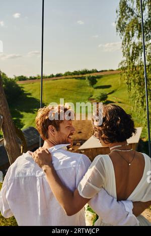 Junge interrassische Paare auf Schaukel in malerischer Landschaft, ländliche Hochzeit Stockfoto