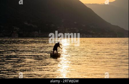 Bei Sonnenuntergang, inmitten der Berge, fischt ein Mann in einem kleinen Boot in der Bucht. Stockfoto