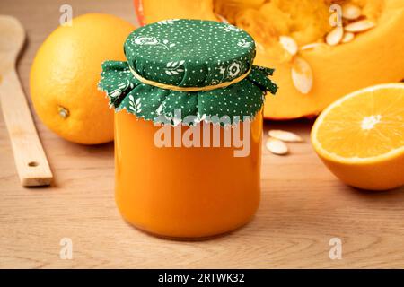 Glas mit hausgemachtem orangen Kürbis und Orangenmarmelade aus nächster Nähe vor einem frischen Kürbis Stockfoto