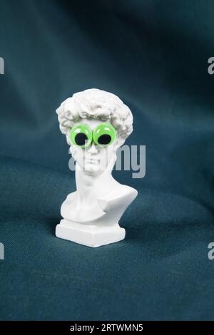 Eine Büste Davids, die auf einem welligen grünen Vorhang mit gefälschten, ausbauchenden Augen aufragt. Comic-Szenographie. Stillleben in minimalen Farben Stockfoto