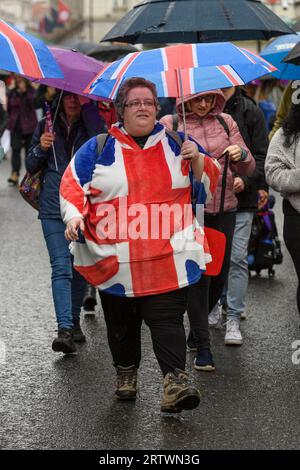 Eine Frau, die ein Union Jack-Top trägt und einen passenden Regenschirm hält, spaziert im Regen entlang Piccadilly Teil der Menge, um König Karl II. Zu beobachten Stockfoto