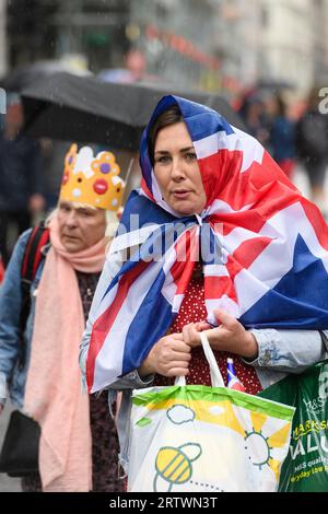 Eine Frau, die eine Union-Jack-Flagge trägt, läuft im Regen auf einem überfüllten Piccadilly, um die Krönung von König Karl III. Zu beobachten. Piccadilly, London, Großbritannien. 6. Mai Stockfoto