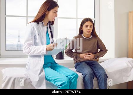 Kindermädchen, das in der Arztpraxis sitzt und während der ärztlichen Untersuchung in der Klinik auf ihren Magen zeigt. Stockfoto