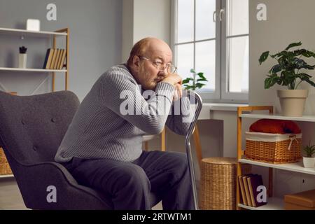 Trauriger einsamer älterer Mann, der mit seinem Stock im Sessel sitzt Stockfoto