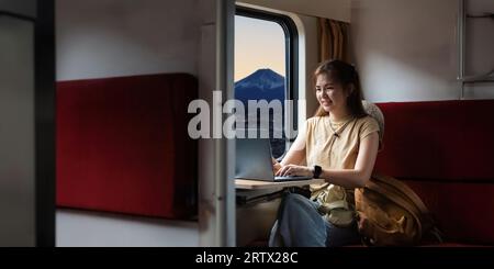 Reisende junge Frau reist im Zug. Arbeiten Sie mit dem Laptop, während Sie im Inneren sitzen. Reisende Touristen haben kleine Reise fuji als Hintergrund Stockfoto