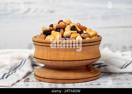 Gemischte Nüsse in Holzschale. Nüsse auf weißem Holzgrund. Gemischte Nüsse, zubereitet mit Haselnüssen, Mandeln, Cashews, Pistazien, Pistazien und Trauben Stockfoto