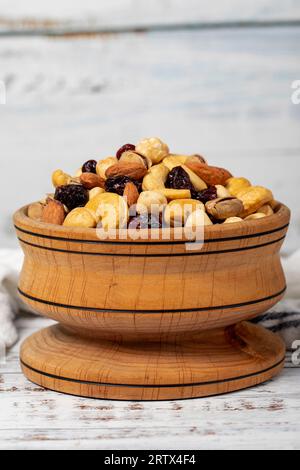 Gemischte Nüsse in Holzschale. Nüsse auf weißem Holzgrund. Gemischte Nüsse, zubereitet mit Haselnüssen, Mandeln, Cashews, Pistazien, Pistazien und Trauben. Schließen Stockfoto