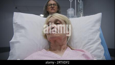 Ältere Frau liegt auf der Bahre, spricht mit reifer Ärztin. Der Arzt bringt den Patienten nach der Operation auf die Krankenhausstation in den modernen Flur des medizinischen Zentrums. Medizinisches Personal am Arbeitsplatz im Krankenhaus. Stockfoto