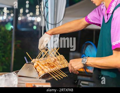 Trader Flip Würstchen Spieße grillen auf Street Food Markt in der Nacht. Stockfoto