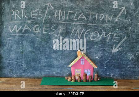 Steigende Mieten, Heizkosten und Preise für Wohnungen, Modellhaus mit gestapeltem Geld vor der Tafel mit Finanzdiagrammen. Kostenloser Kopierplatz Stockfoto