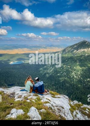 Junges Paar mit Hund, der auf dem Mountain Top sitzt Stockfoto