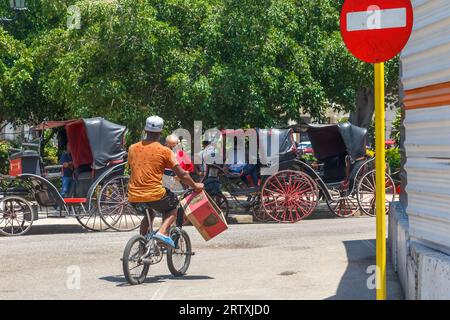 Havanna, Kuba, 2023, Ein kubanischer Mann fährt Ein Fahrrad auf einer Straße in der Stadt. Er trägt eine Pappschachtel. Stockfoto