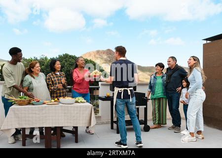 Generationenübergreifende Freunde, die Spaß beim Grillen auf dem Dach des Hauses haben - fröhliche, multirassische Menschen, die zusammen kochen Stockfoto