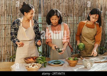 Glückliche südostasiatische Familie, die Spaß dabei hat, das thailändische Speisenrezept zusammen auf der Terrasse des Hauses zuzubereiten Stockfoto