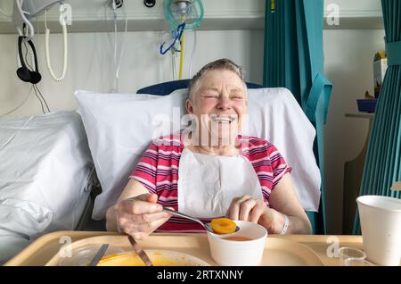 Glückliche ältere Patientin lachend in ihrem NHS Krankenhausbett, London, England, Großbritannien Stockfoto