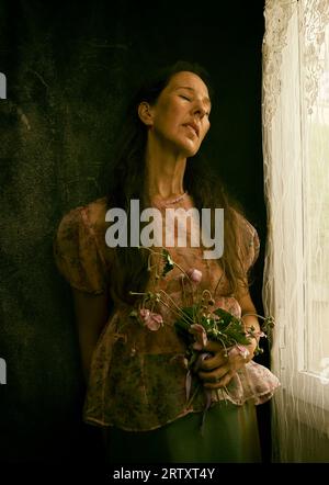 Frau mit Blumenstrauß in der Nähe des Fensters II Stockfoto