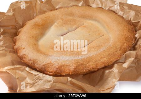 Studio-Aufnahme von einem ganzen Obstkuchen in Backpapier, ausgeschnitten auf weißem Hintergrund - John Gollop Stockfoto