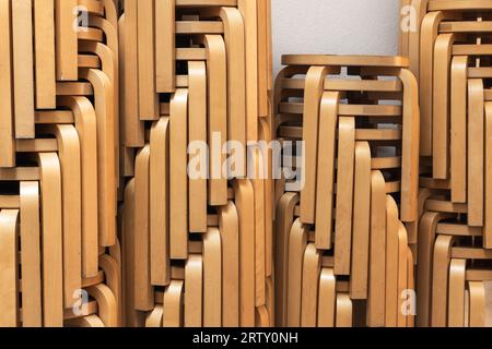 Gestapelte runde Holzstühle aus gebogenem Sperrholz stehen vor einer weißen Wand Stockfoto