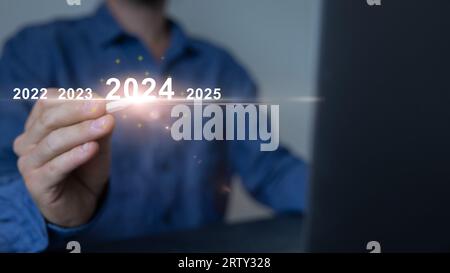 Mann, der auf dem virtuellen Bildschirm die Startschaltfläche für das neue Jahr 2024, das neue Jahr 2024 mit Zielplan, Zielkonzept, Aktionsplan, Strategie, neues Jahr berührt. Stockfoto