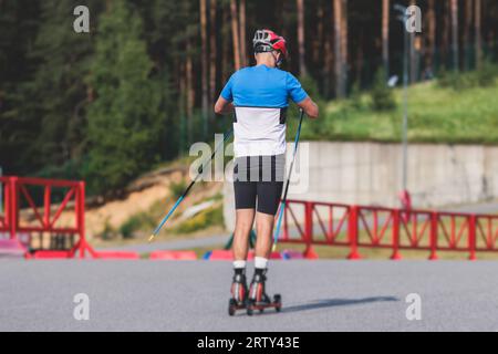 Athleten reiten Rollski auf Asphaltpiste, Gruppe Skierollen im Helm, Langlaufen mit Rollski an einem sonnigen Sommertag, Sportler Ski- Stockfoto