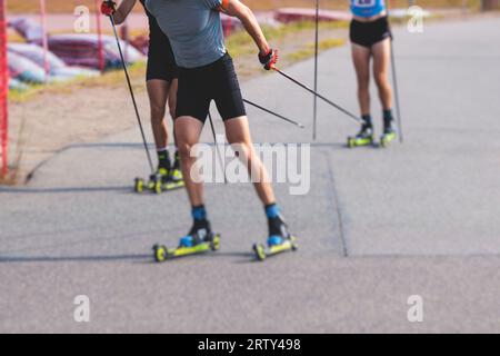 Athleten reiten Rollski auf Asphaltpiste, Gruppe Skierollen im Helm, Langlaufen mit Rollski an einem sonnigen Sommertag, Sportler Ski- Stockfoto