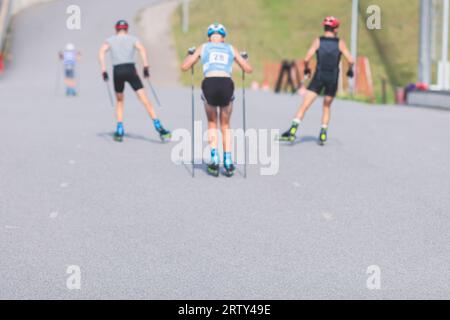 Athleten reiten Rollski auf Asphaltpiste, Gruppe Skierollen im Helm, Langlaufen mit Rollski an einem sonnigen Sommertag, Sportler Ski- Stockfoto