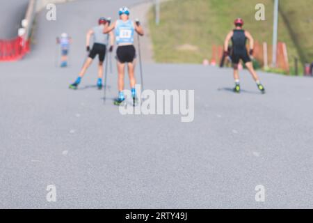 Athleten reiten Rollski auf Asphaltpiste, Gruppe Skierollen im Helm, Langlaufen mit Rollski an einem sonnigen Sommertag, Sportler Ski- Stockfoto