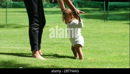 Das süße Baby lehnt sich draußen auf die Beine der Mutter. Entzückendes Kleinkind, das neben der Mutter steht und sich im Freien aufhält Stockfoto