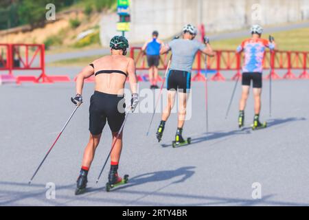 Athleten reiten Rollski auf Asphaltpiste, Gruppe Skierollen im Helm, Langlaufen mit Rollski an einem sonnigen Sommertag, Sportler Ski- Stockfoto