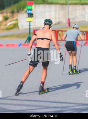 Athleten reiten Rollski auf Asphaltpiste, Gruppe Skierollen im Helm, Langlaufen mit Rollski an einem sonnigen Sommertag, Sportler Ski- Stockfoto