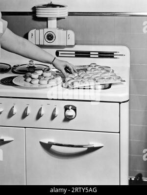 Wisconsin c 1935. Eine Frau überträgt frisch gebackene Kekse, die in ihrem Monarch-Ofen zubereitet werden, auf einen Teller vom Keksblatt. Stockfoto