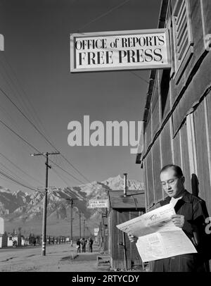 Owens Valley, Kalifornien 1943 Redakteur Roy Takeno las eine Kopie der Manzanar Free Press vor dem Zeitungsbüro im Manzanar war Relocation Center im Owens Valley, Kalifornien. Die Manzanar Free Press wurde im April 1942 von ehemaligen Journalisten ins Leben gerufen, die schließlich zu einem Umzugszentrum für Japaner wurden. In der ersten Ausgabe, die am 22. Juli 1942 gedruckt wurde, heißt es: „Wir möchten noch einmal wiederholen, dass die Freie Presse dem Volk von Manzanar gehört, dass sie nicht nur das Sprachrohr der Regierung ist, sondern die Meinung der Evakuierten in den s zum Ausdruck bringt Stockfoto