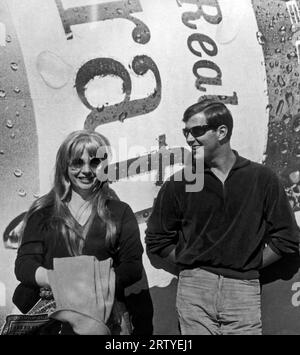 Vereinigte Staaten um 1960 Ein Paar mit Sonnenbrille steht vor einer großen Werbung für ein Bier vom Fass. Stockfoto